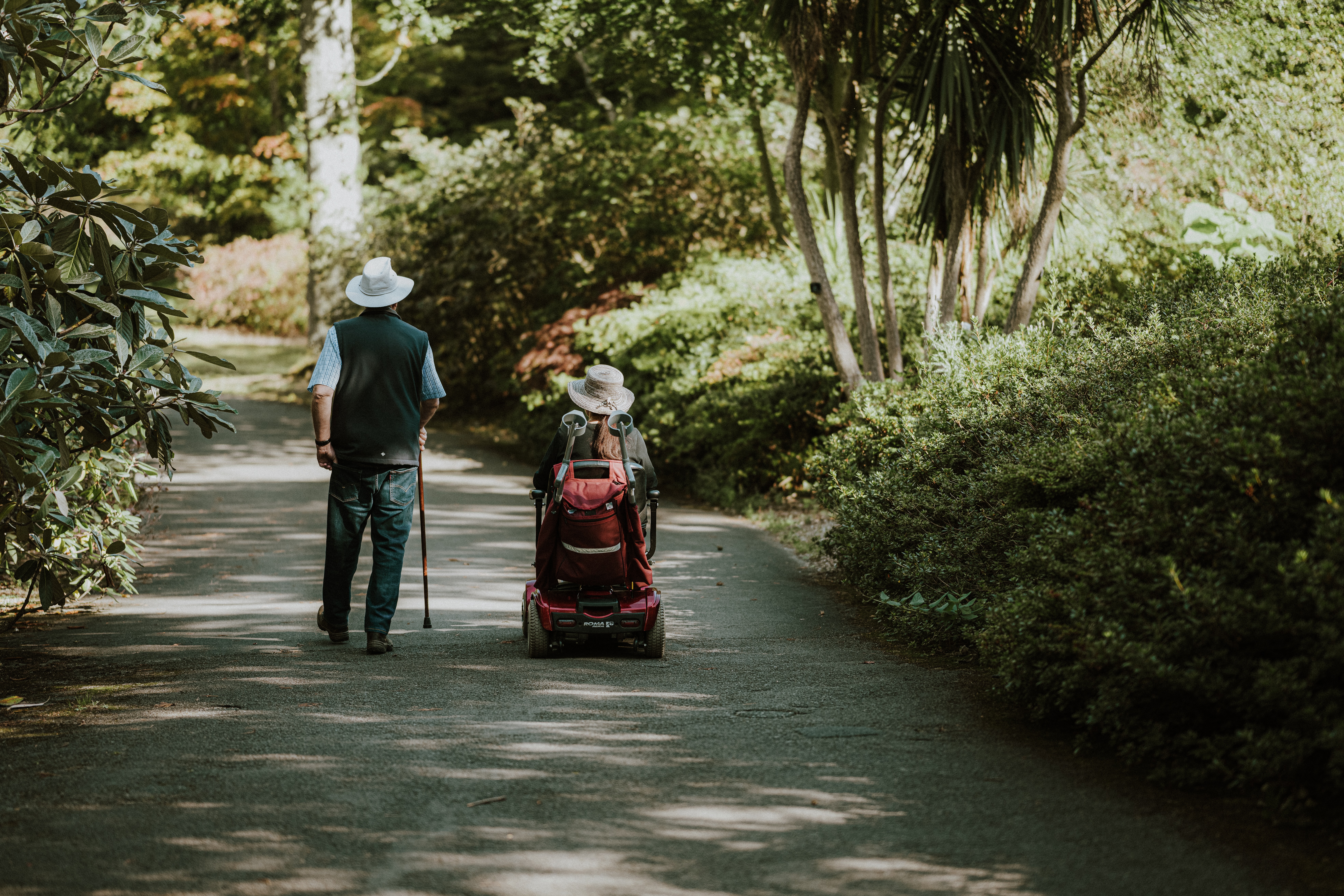 Man walking using a mobility aid cane next to a woman in a powerchair. Man walking using a mobility aid cane next to a woman in a powerchair.