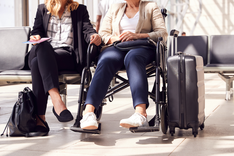 Two women sitting in an airport, one in a wheelchair, with baggage.