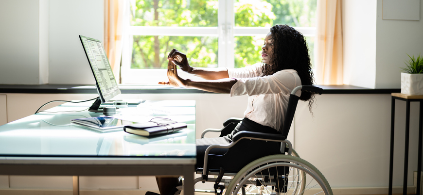 Disabled woman stretches while sitting in a wheelchair at a desk