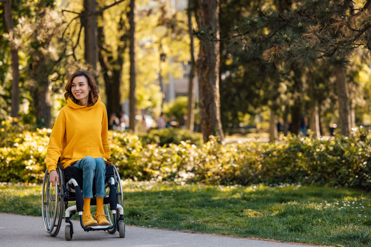 Woman in yellow in a wheelchair on the sidewalk outside of a park