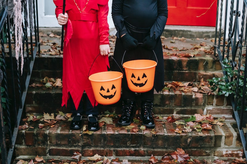 Two children standing on brick stairs holding pumpkin candy pails, one dressed in red the other in black. 